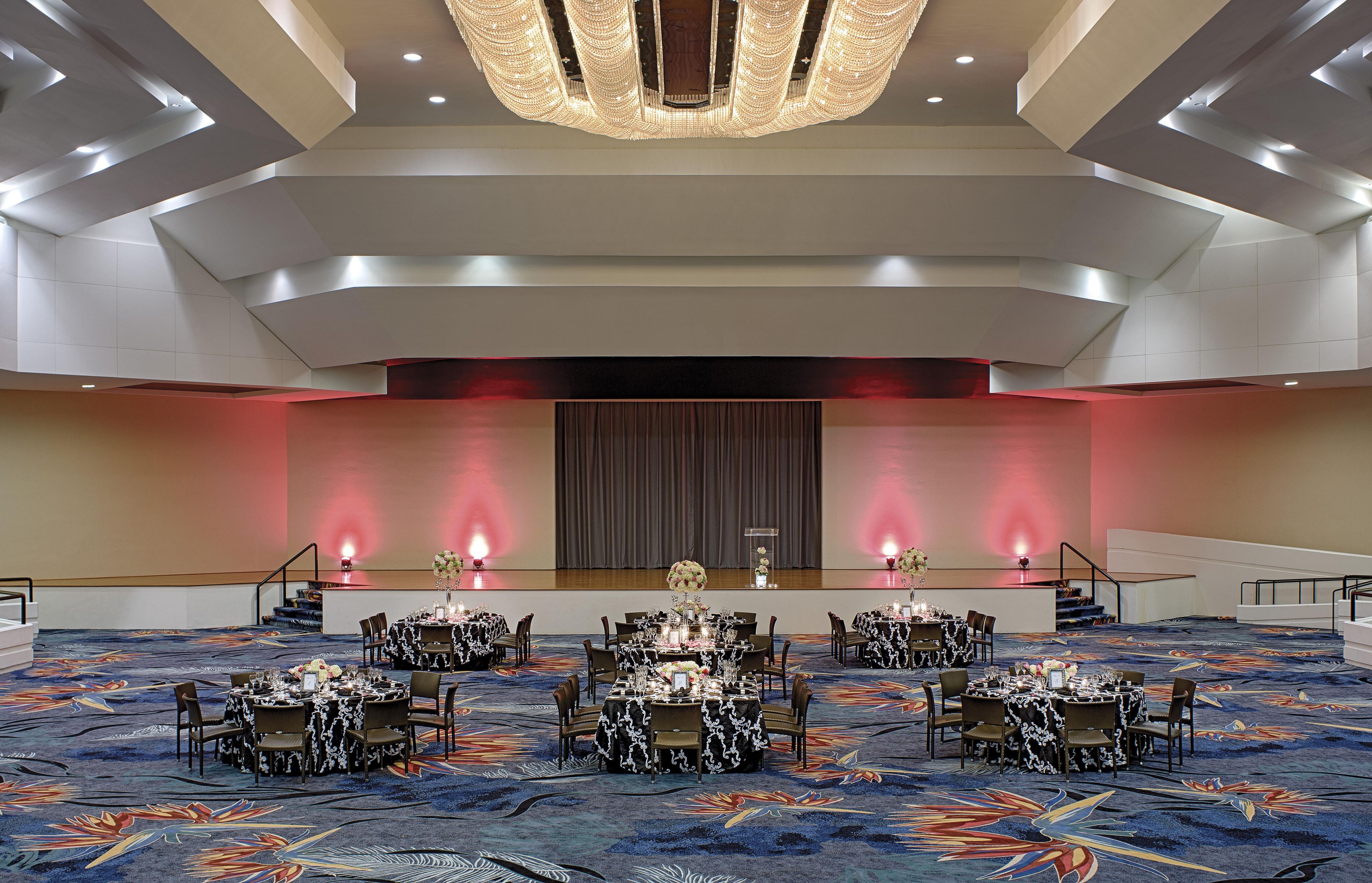 A spacious banquet hall with tiered seating, a central stage, and a modern chandelier.