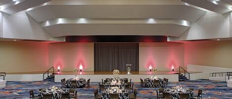 A spacious banquet hall with tiered seating, a central stage, and a modern chandelier.