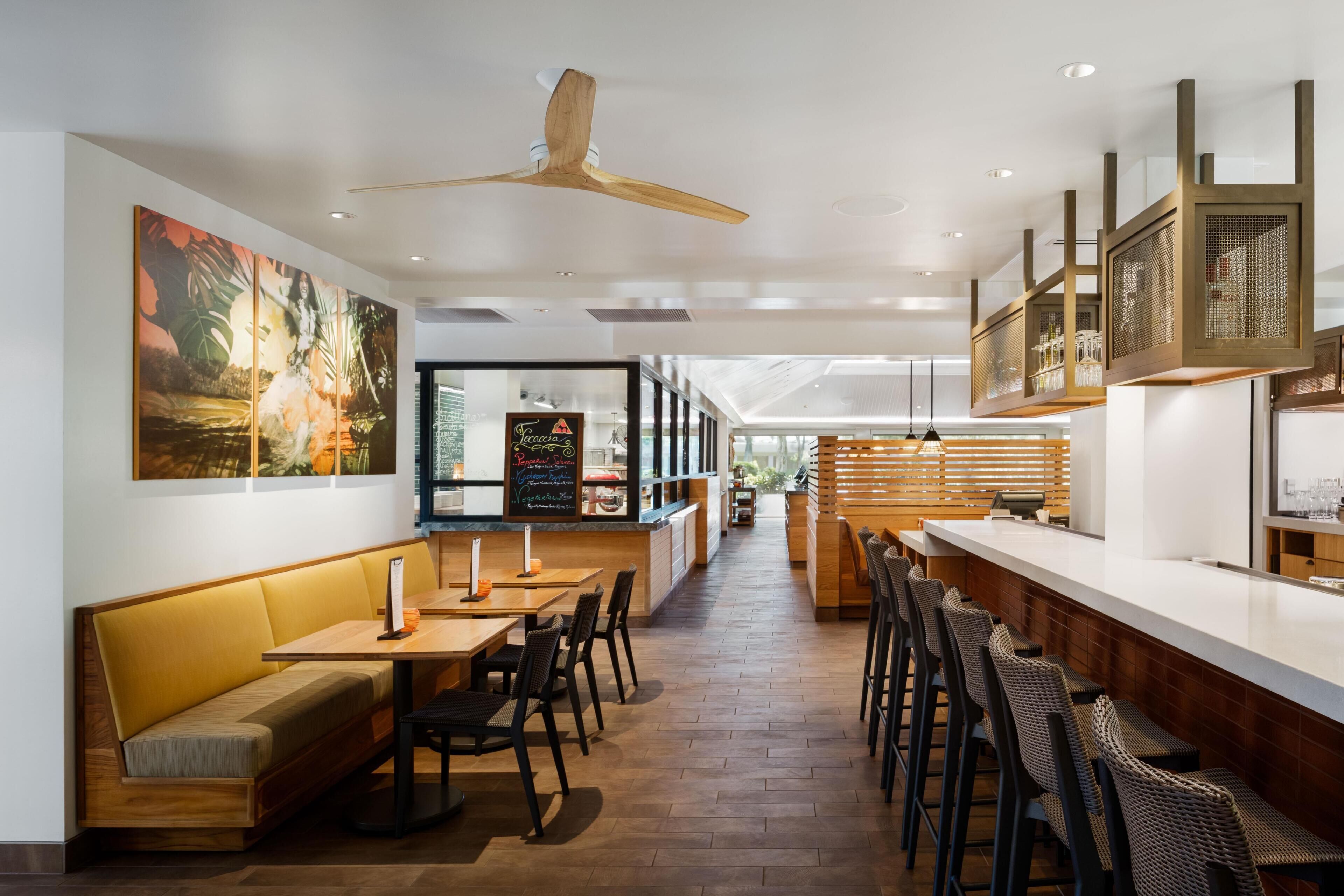 A modern restaurant interior with wooden furniture, a bar area, and a large painting on the wall.