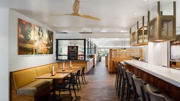 A modern restaurant interior with wooden furniture, a bar area, and a large painting on the wall.