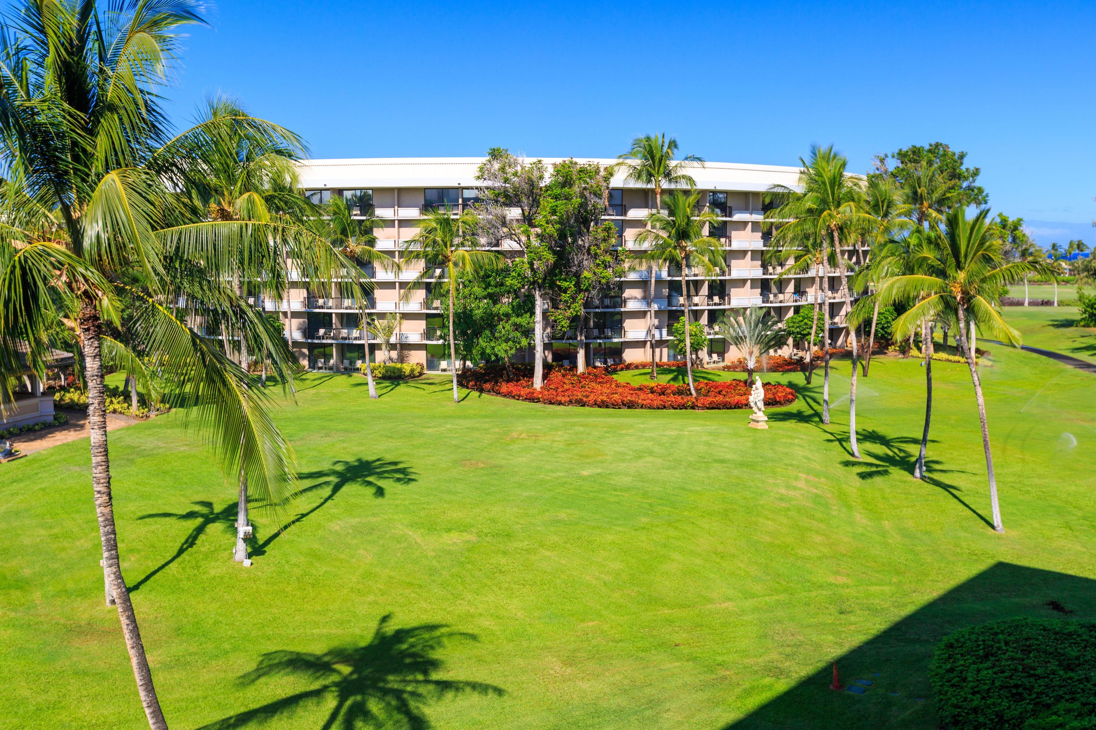 A multi-story hotel with a well-maintained lawn and palm trees.