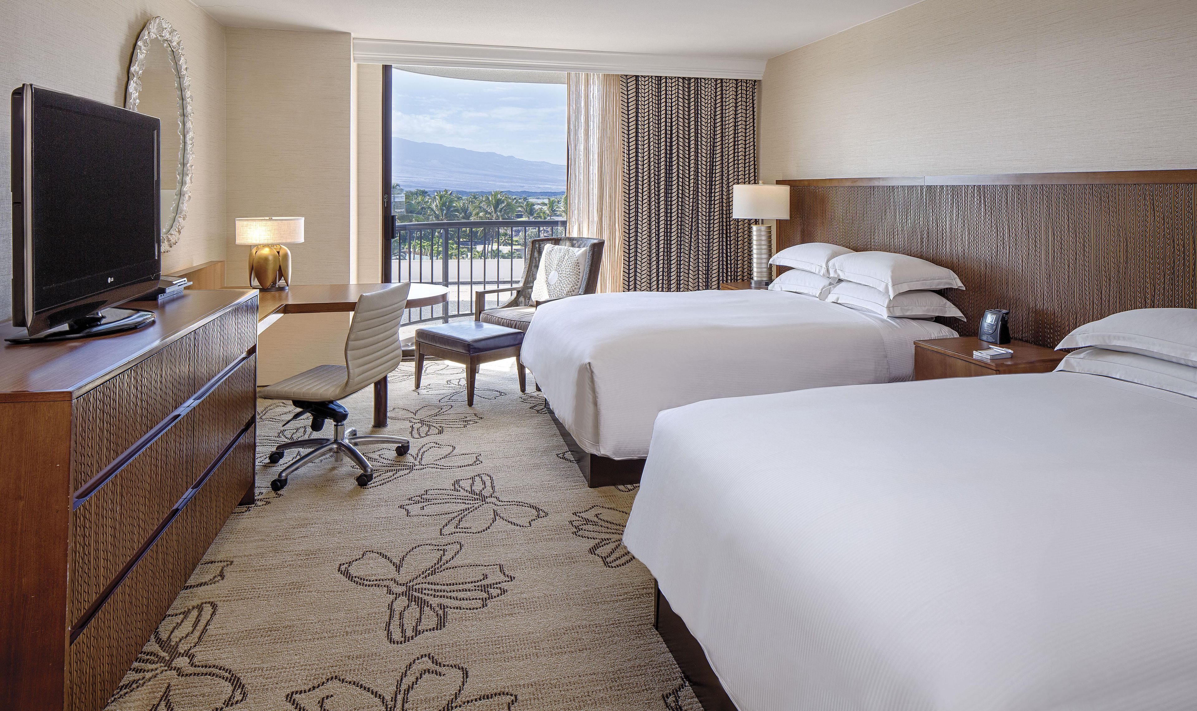 A hotel room with two beds, a desk with a television, a chair, and a view of the outdoors.
