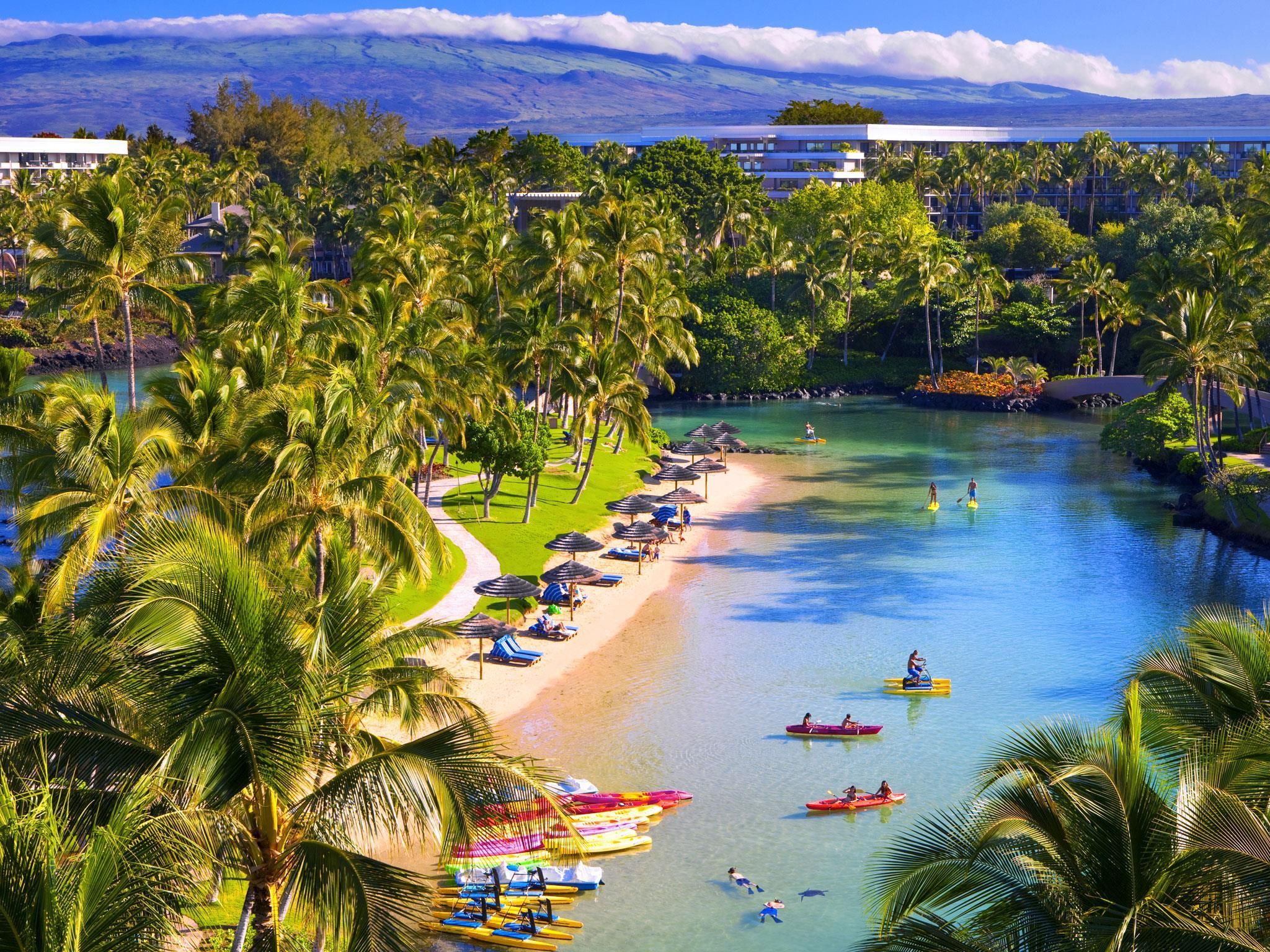 A resort with a beach, palm trees, and a clear view of a mountain range.