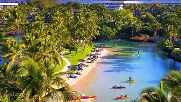 A resort with a beach, palm trees, and a clear view of a mountain range.