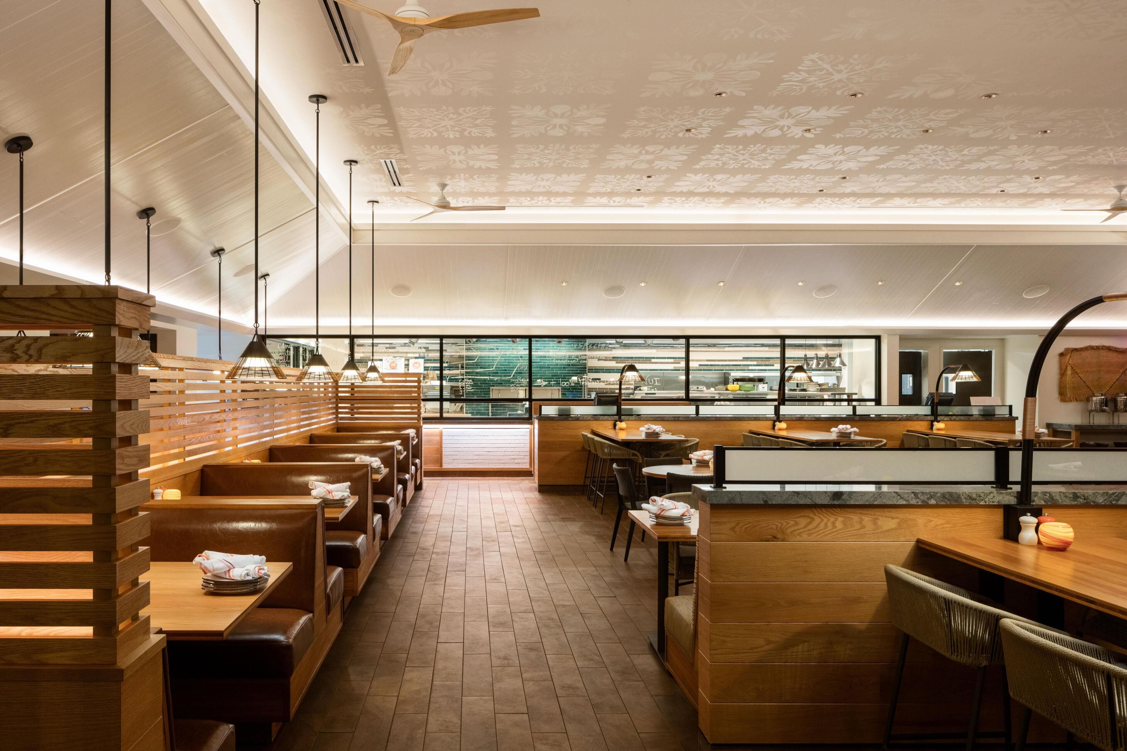 A restaurant with wooden booths, a bar area, and a view of the kitchen through large windows.