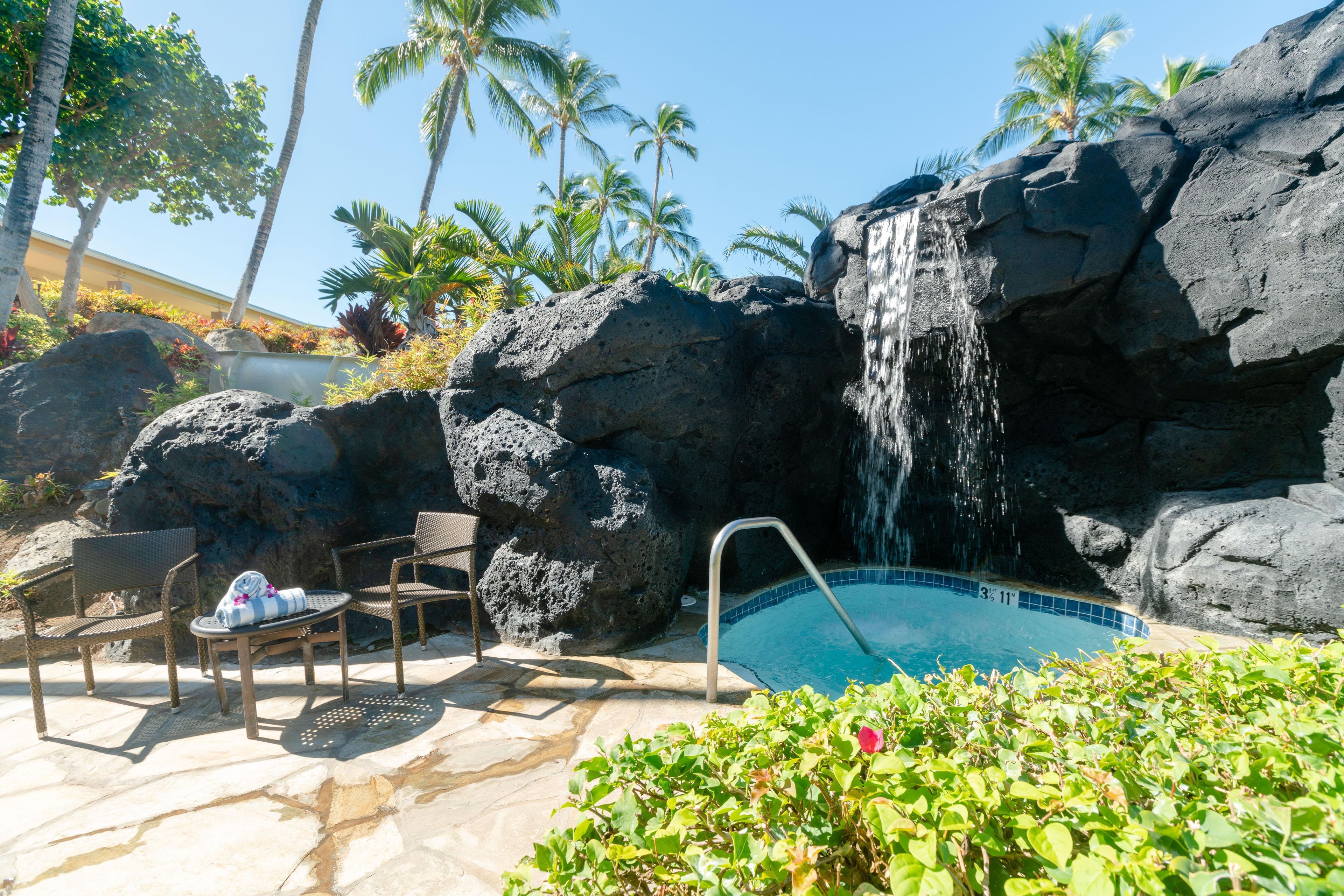 Zona de piscina con cascada, rodeada de rocas y palmeras.