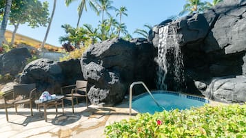 Ein Poolbereich mit Wasserfall, umgeben von Felsen und Palmen.