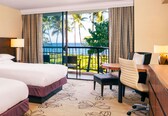 A hotel room with two beds, a desk, a chair, a small table, and a view of the ocean.