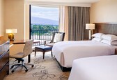 A hotel room with a bed, a desk, a chair, a balcony with a view, and a patterned curtain.