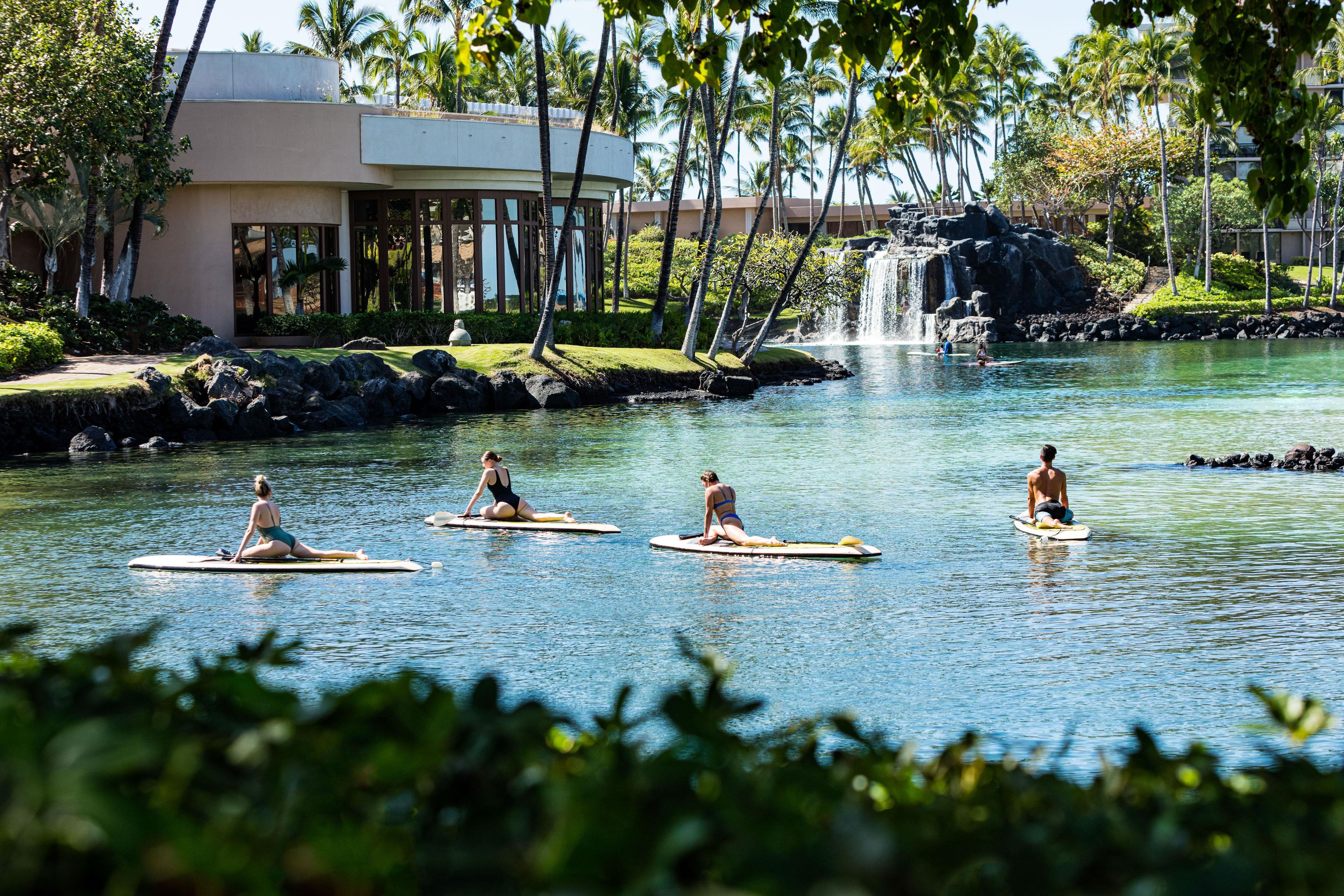 A resort with a water body, palm trees, and a building with a waterfall.