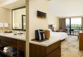 A hotel room with a large bed, a bathroom with a sink and mirror, a coffee maker, and a balcony with a view.