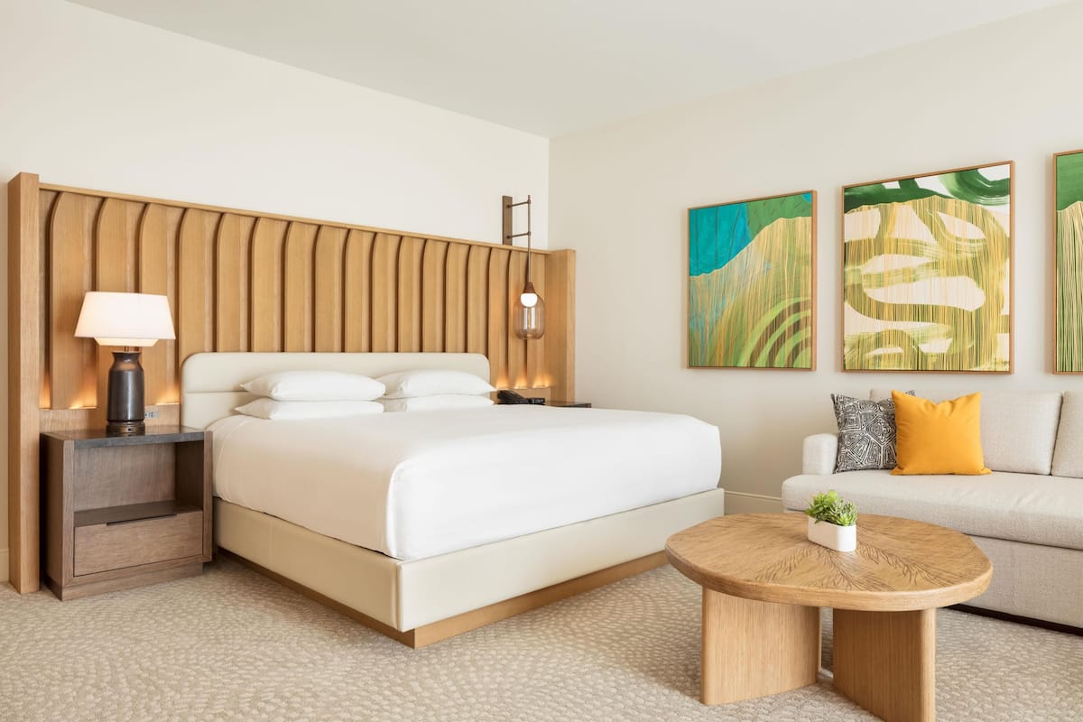 Une chambre d’hôtel moderne, dotée d’un grand lit, de tables de chevet, d’une table basse ronde et d’œuvres d’art accrochées aux murs.