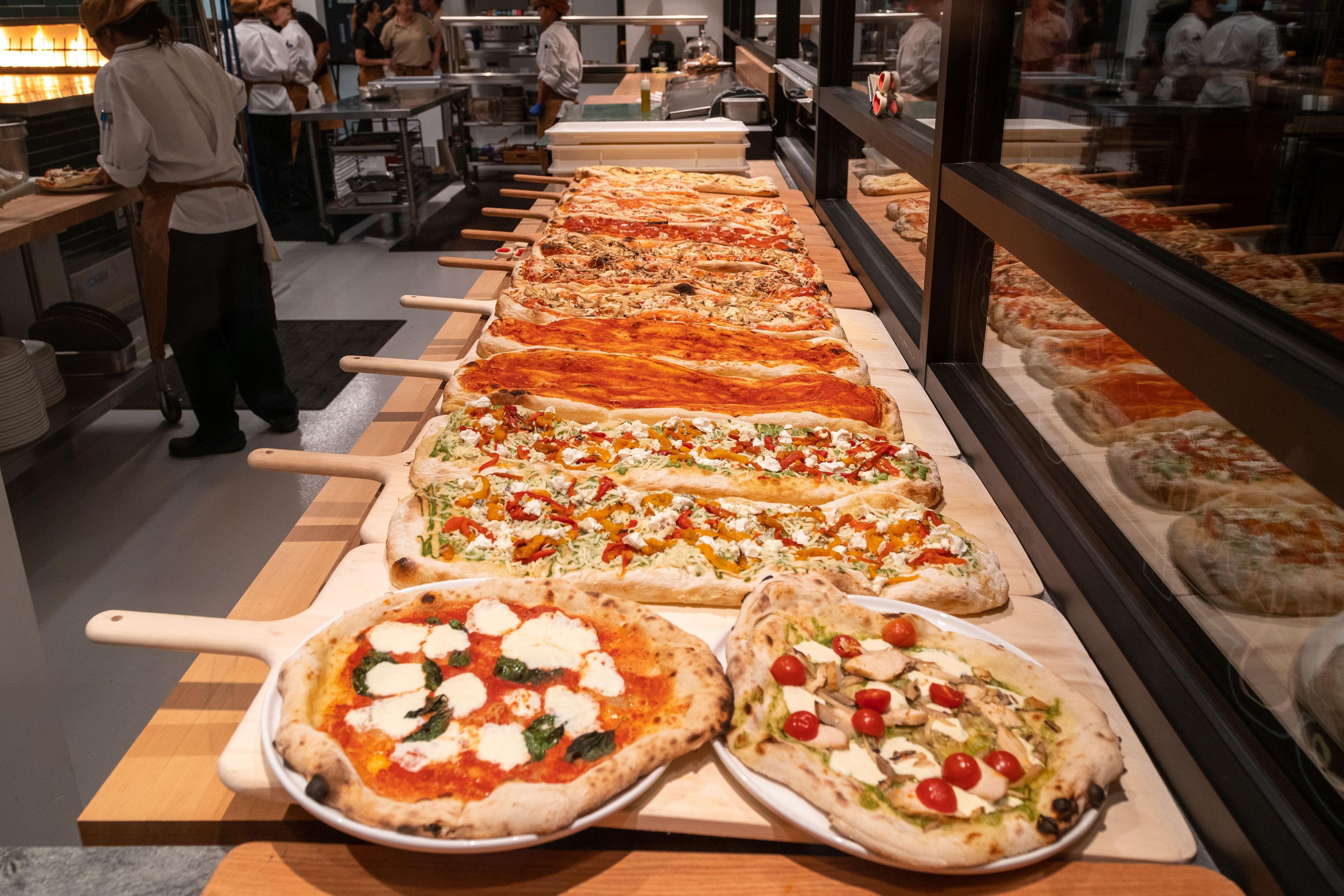 Egy sor pizza, melyeket fából készült tálalódeszkákra helyeztek, egy konyhában.
