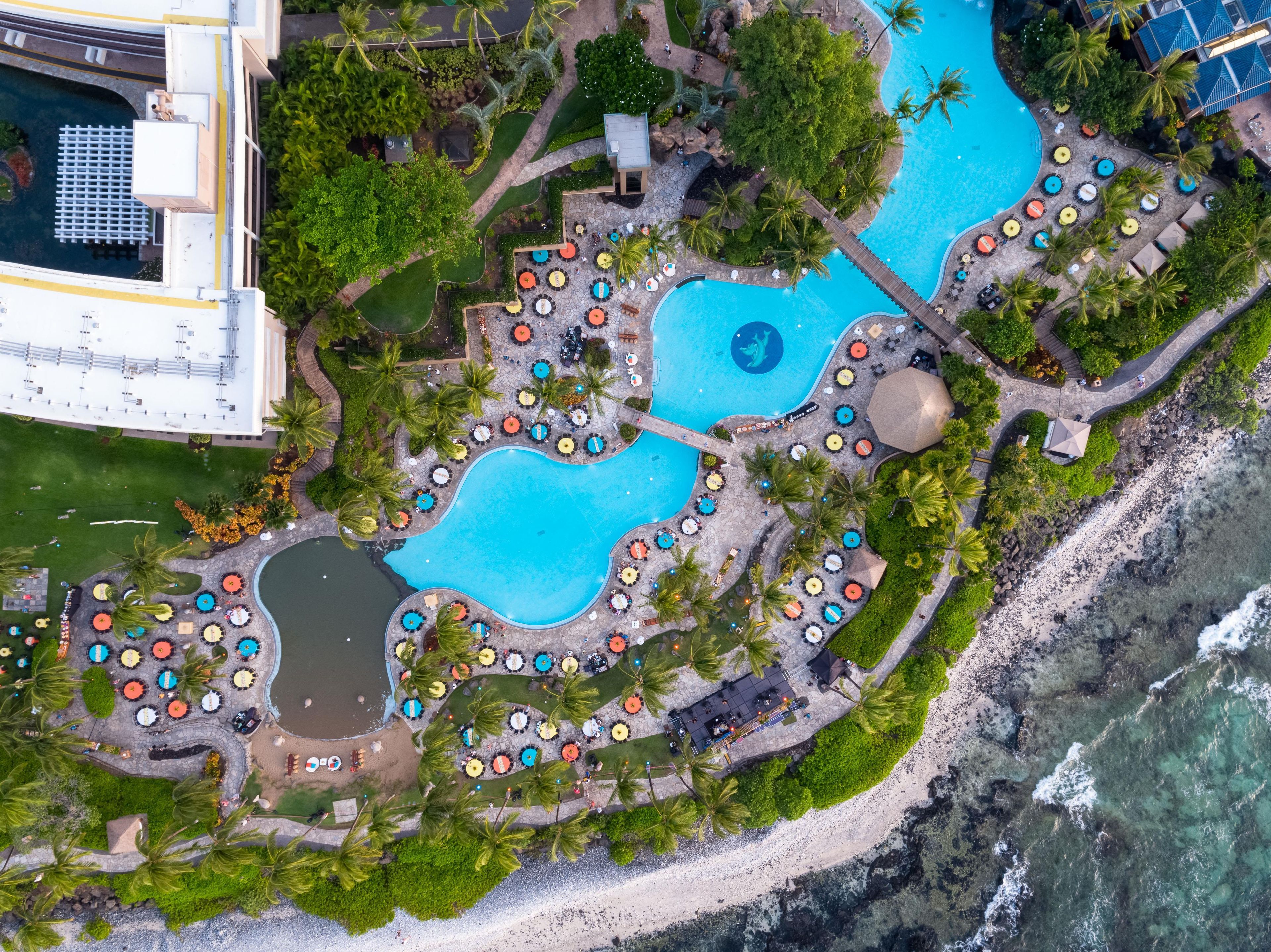 Luchtbeeld van een resort met meerdere zwembaden, ligbedden en palmbomen.