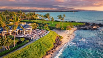 A coastal resort with a dining area, palm trees, and a view of the ocean.