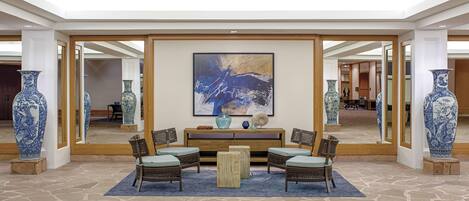 A lobby with a stone floor, a central seating area with chairs and a table, and large vases on either side.