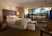 A hotel room with a large bed, a balcony with a view of the ocean, and a television.