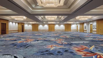 Une grande salle de conférence dotée d’un tapis à motifs, de lambris en bois et de plusieurs lustres.