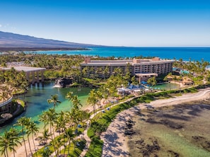 A resort with a large building, a beach, and a clear blue ocean. - Hilton Waikoloa Village (Waikoloa)
