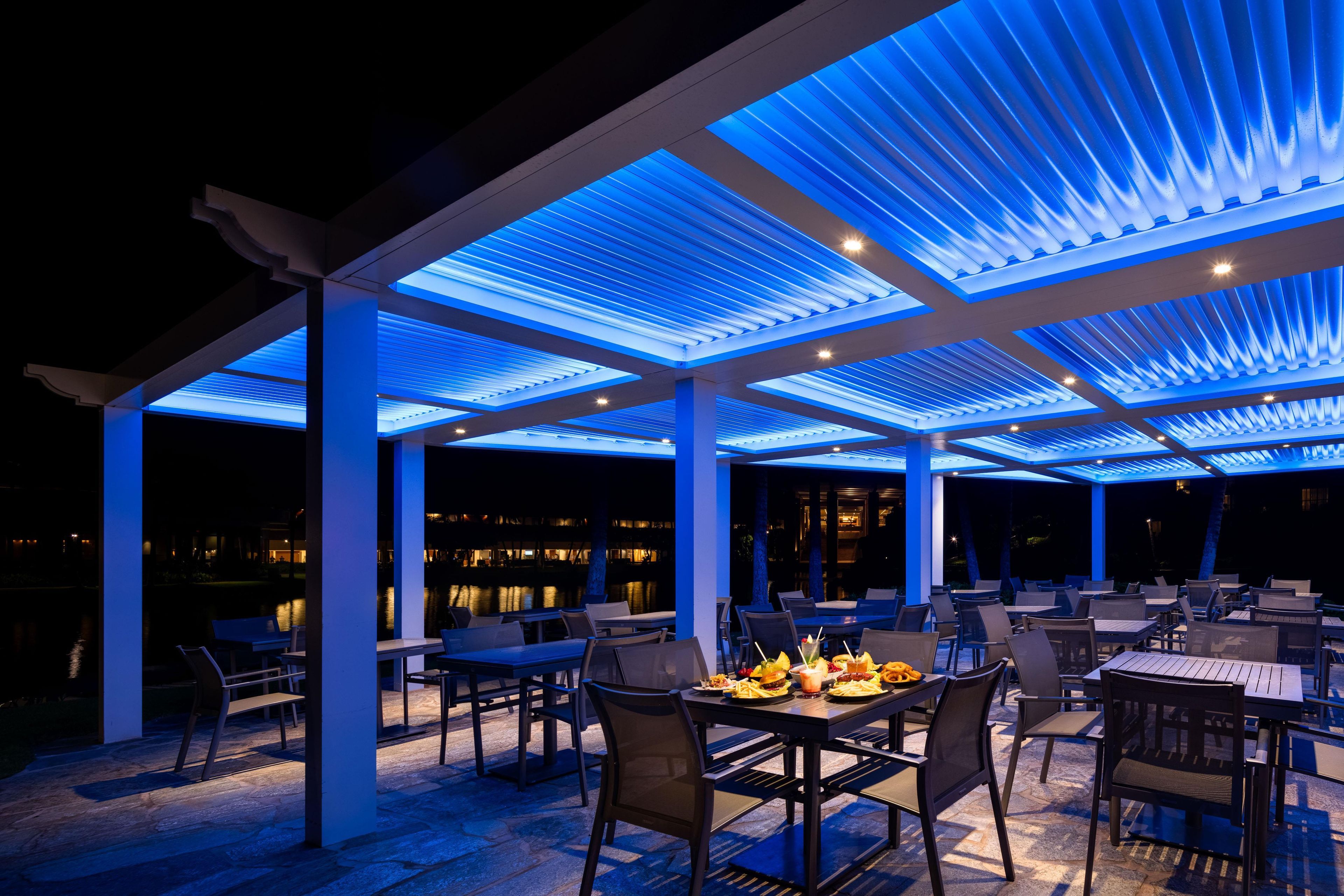 Un espace extérieur aménagé en terrasse avec des tables et des chaises, une piscine en arrière-plan et un ciel nocturne.
