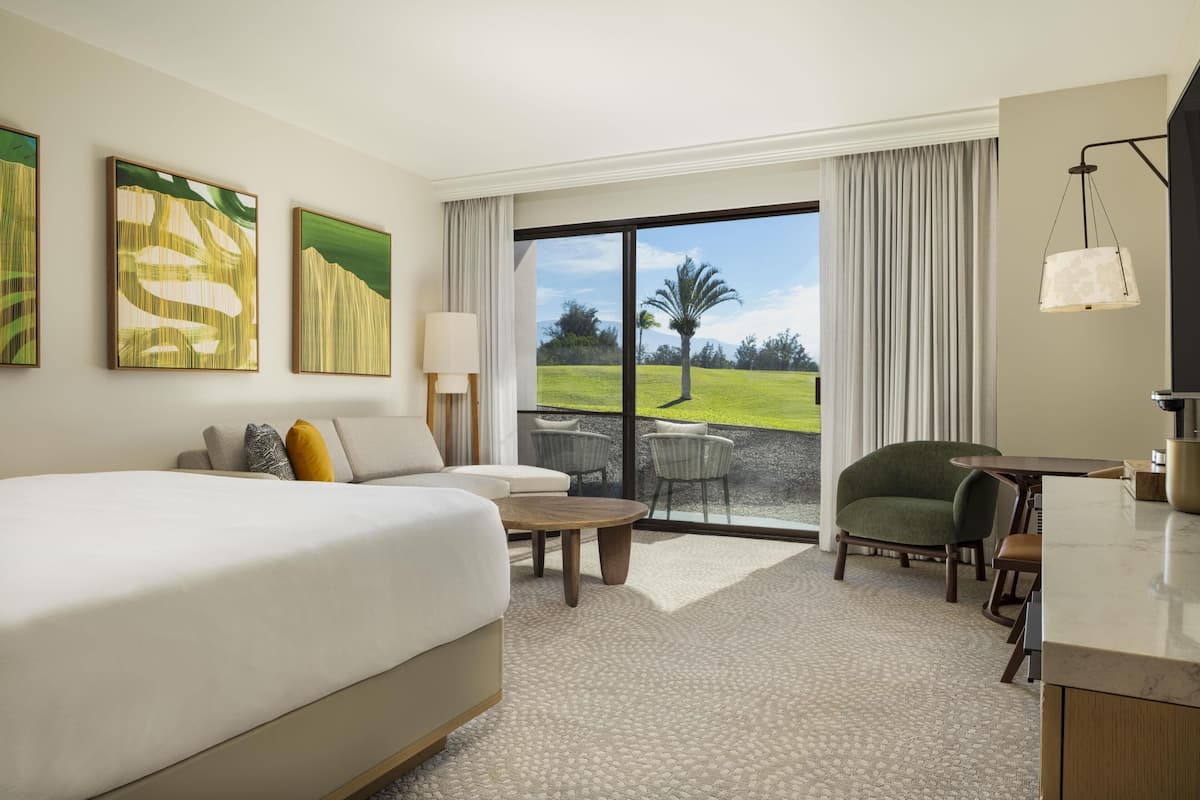 Une chambre d’hôtel avec un grand lit, un canapé, une table à manger, une chaise et une vue sur un espace verdoyant, visible à travers une porte vitrée.