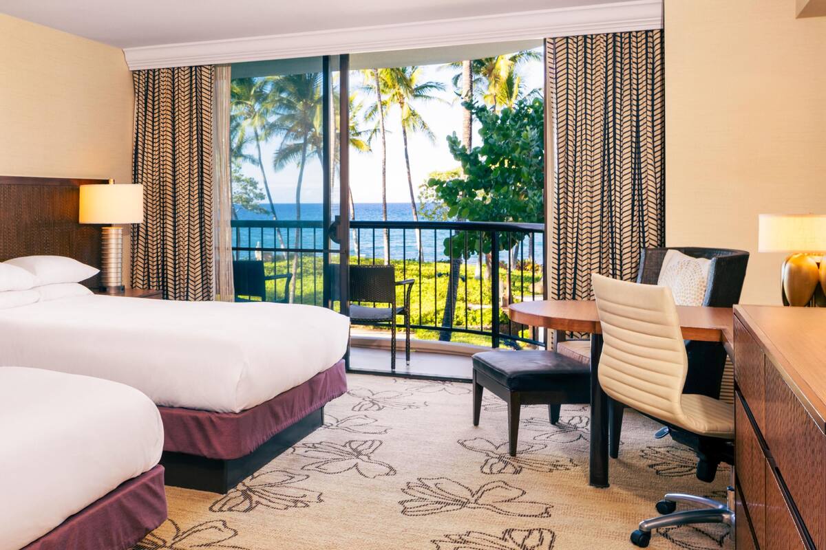 A hotel room with a balcony, a bed, a desk, a chair, and a view of the ocean.