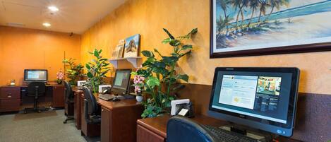 Oficina de hotel con varios puestos de trabajo, un cuadro de una playa y un monitor de computadora mostrando un sitio web.