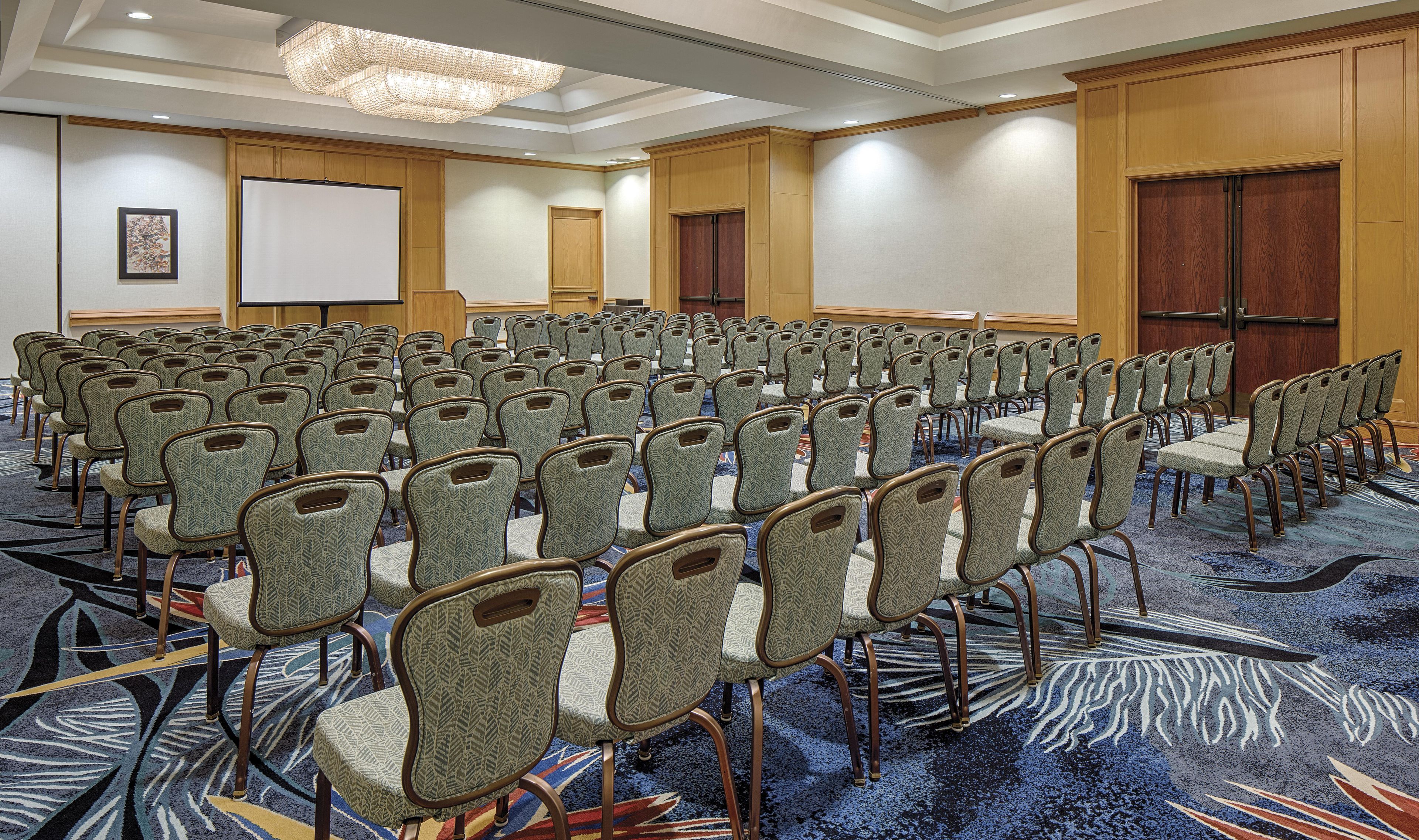 A conference room with rows of chairs, a projector screen, and a carpeted floor.