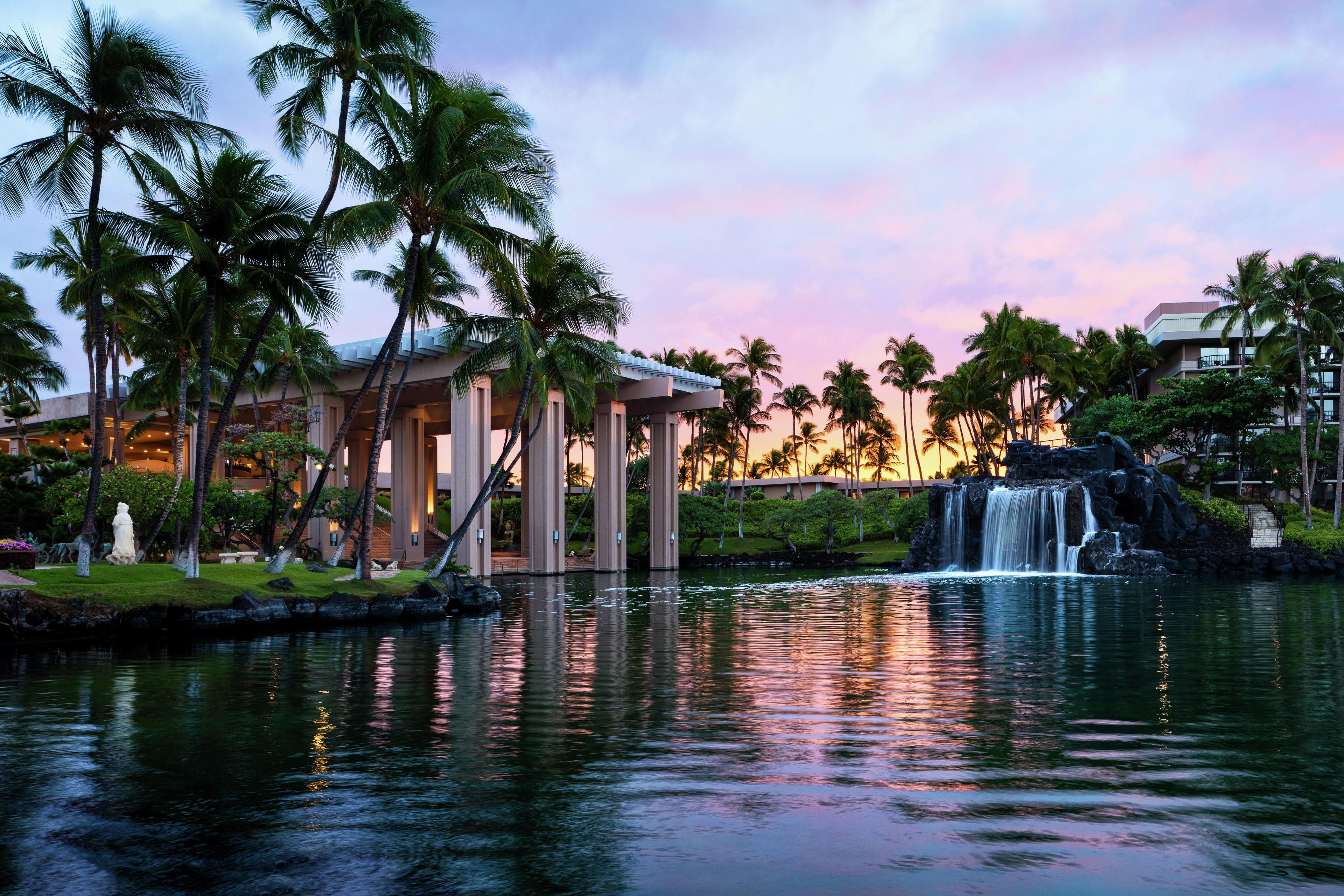 A resort with a water feature, palm trees, and a building with a covered area.
