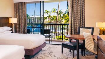 A hotel room with a bed, a desk, a chair, and a view of a pool and palm trees.