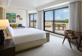 A hotel room with a bed, a desk, a chair, a balcony with a table and chairs, and a large window.