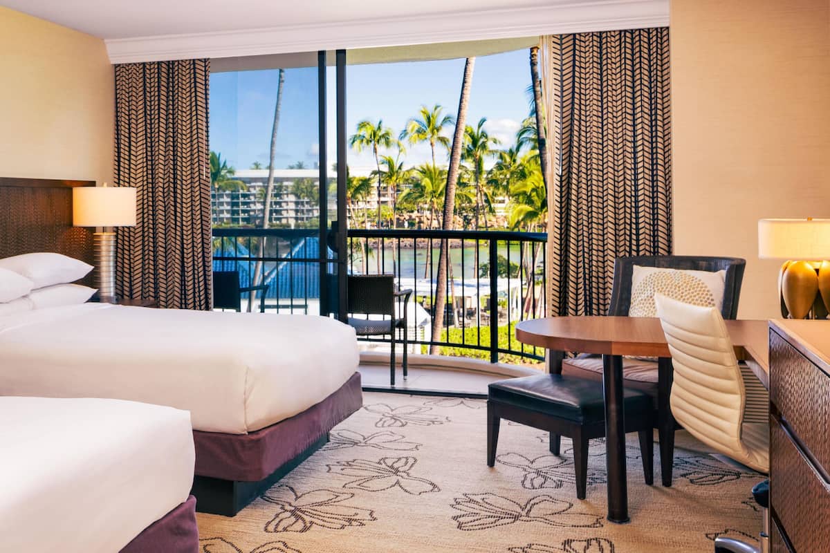 A hotel room with a bed, a desk, a chair, and a view of palm trees and a pool.