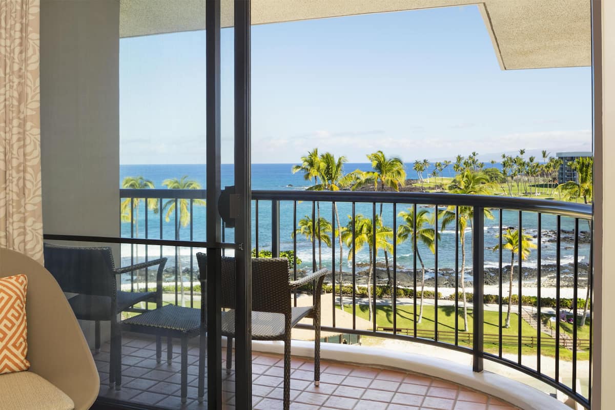A balcony with a view of the ocean, palm trees, and a beach.