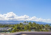 A hotel balcony with a view of a parking lot, palm trees, and a distant mountain range.
