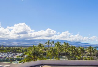 A hotel balcony with a view of a parking lot, palm trees, and a distant mountain range.
