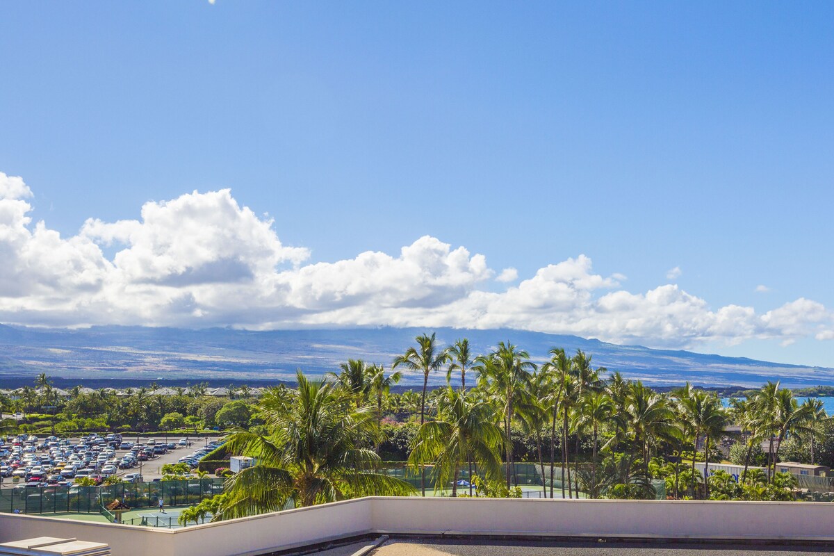 A hotel balcony with a view of a parking lot, palm trees, and a distant mountain range.