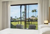 A hotel room with a large window, a bed, a chair, a small table, and a lamp.