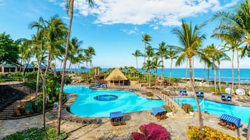 A resort with a large swimming pool, palm trees, and a view of the ocean.