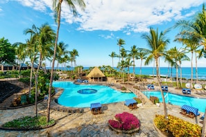 A resort with a large swimming pool, palm trees, and a view of the ocean.