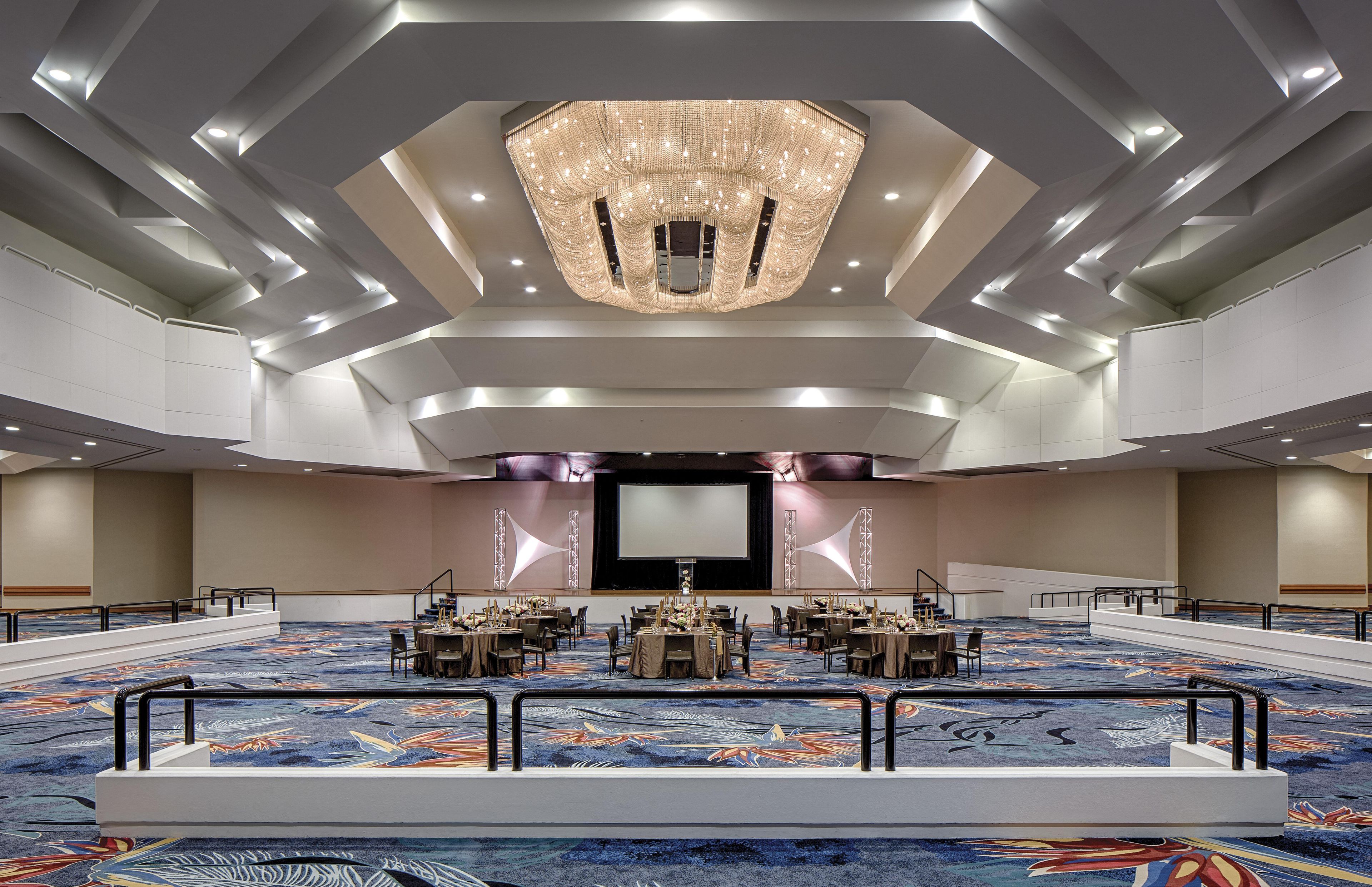 A large conference room with a high ceiling, a central chandelier, and a carpeted floor.