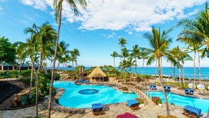 A resort with a large swimming pool, palm trees, and a view of the ocean.