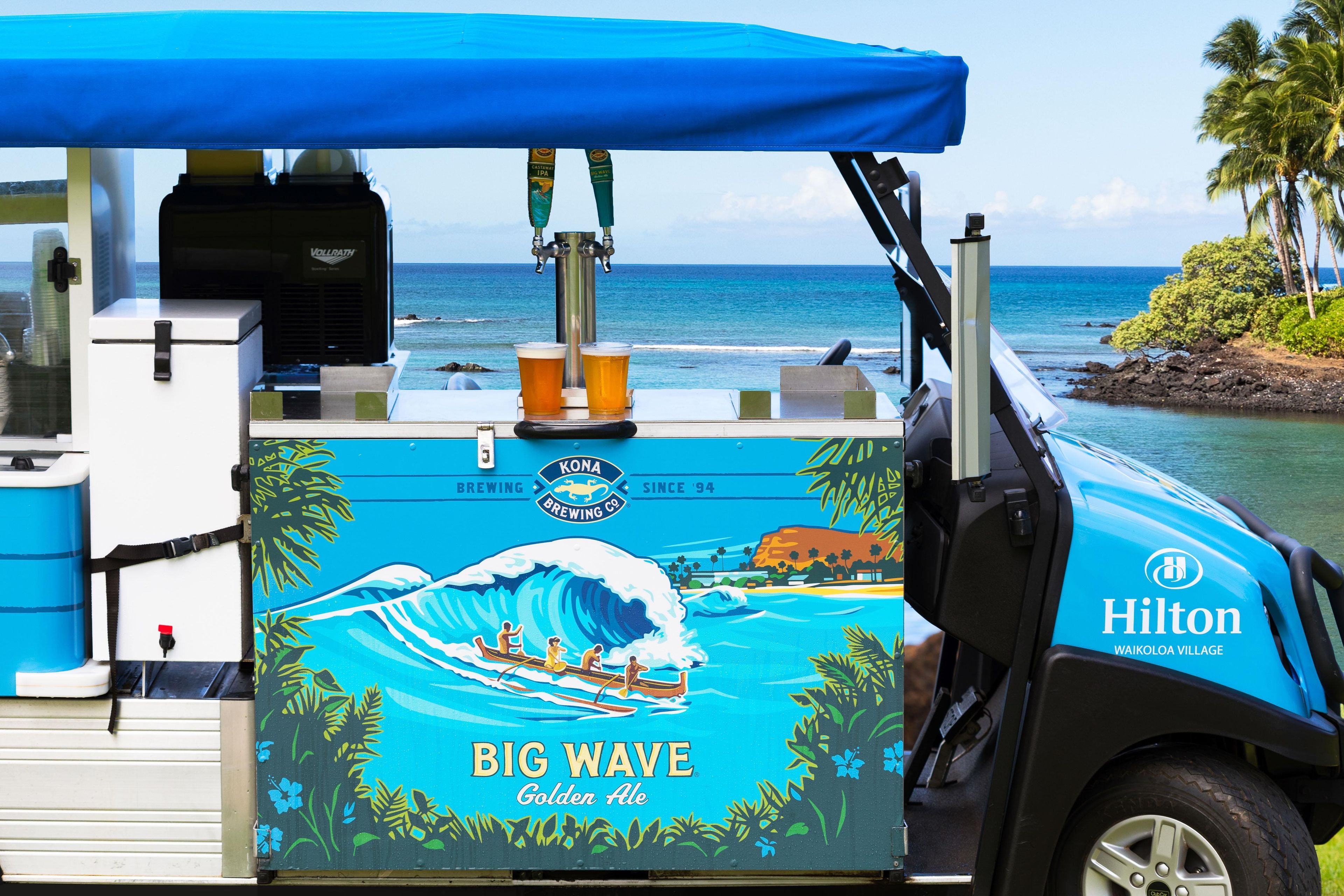 Eine mobile Bar im tropischen Stil, mit Branding für Big Wave Golden Ale, auf einem Boot mit Blick auf den Ozean.