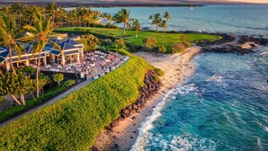A coastal resort with a dining area, palm trees, and a view of the ocean.