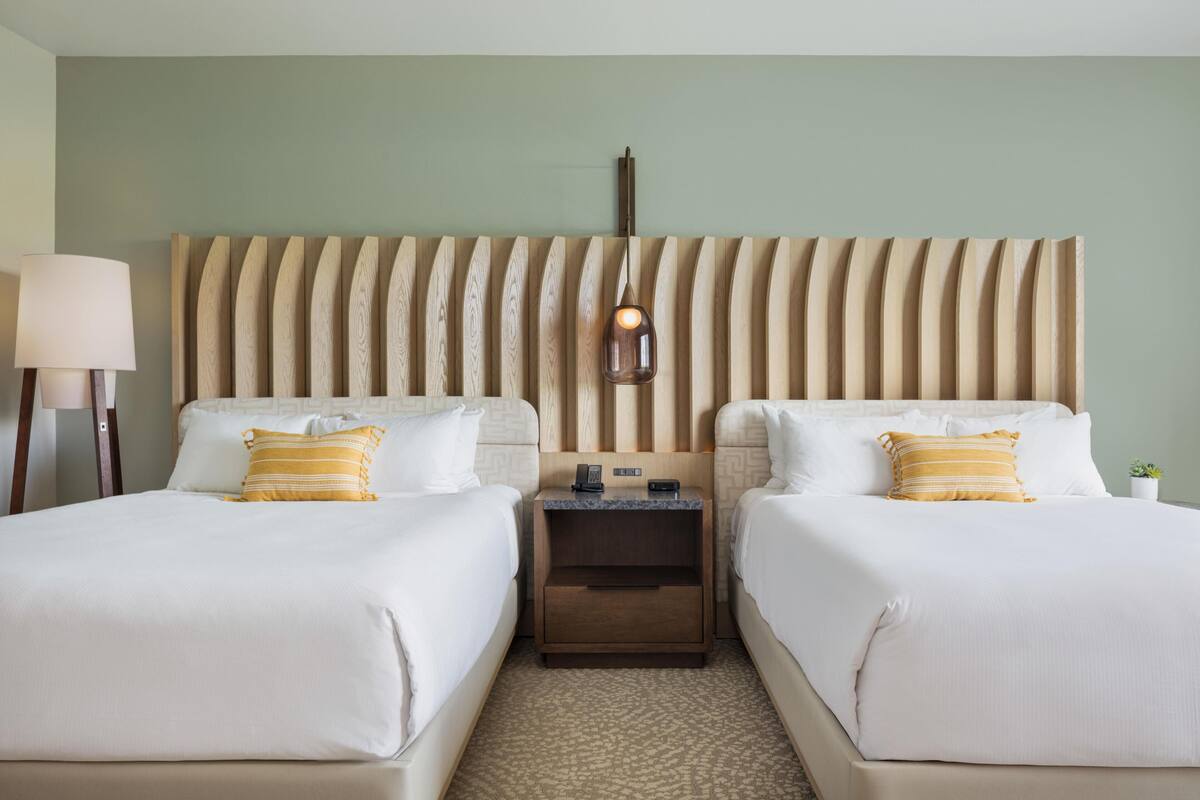 Une chambre d’hôtel avec deux lits, une table de chevet, une lampe et un luminaire fixé au mur.