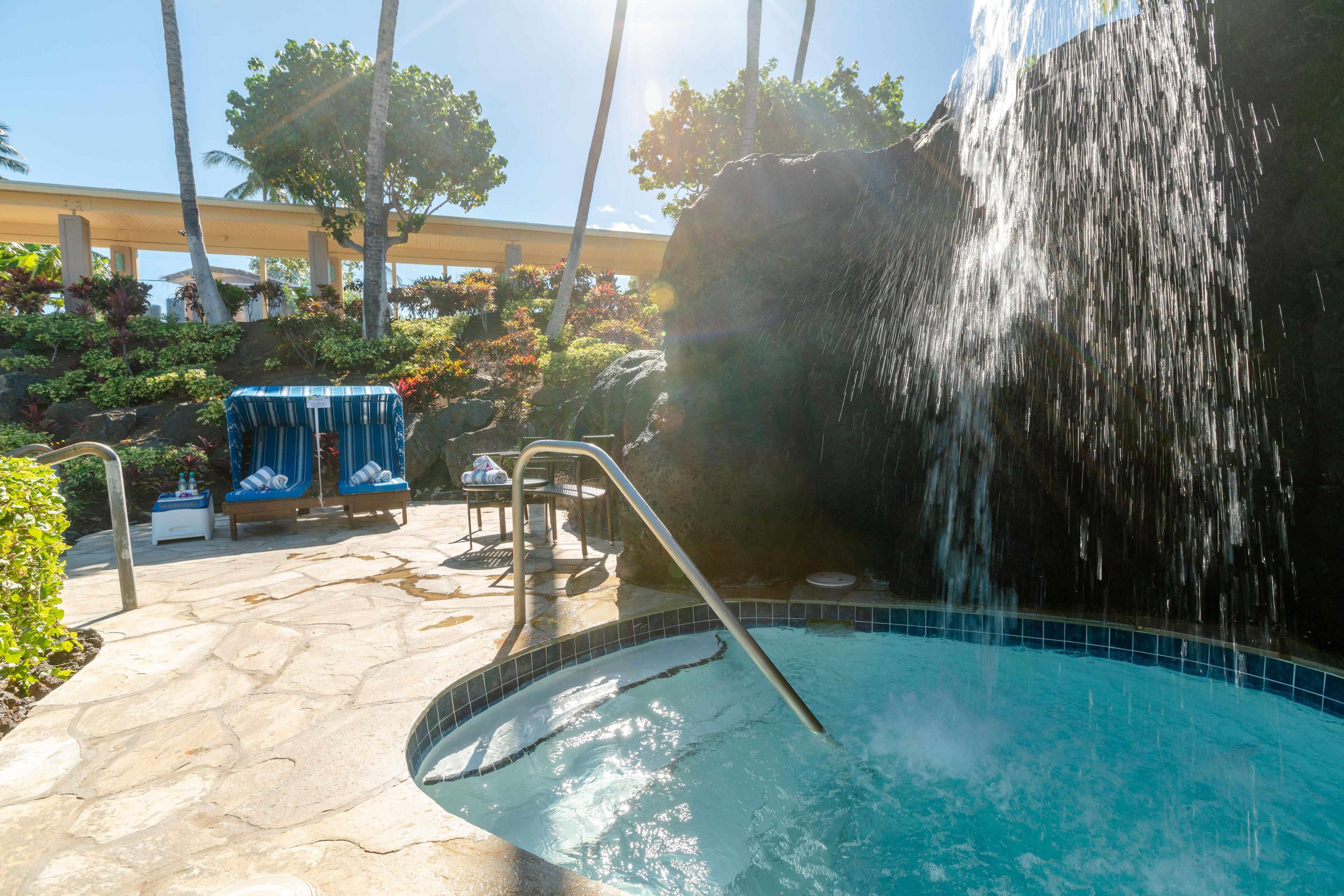 A pool area with a waterfall feature, lounge chairs, and a covered seating area.