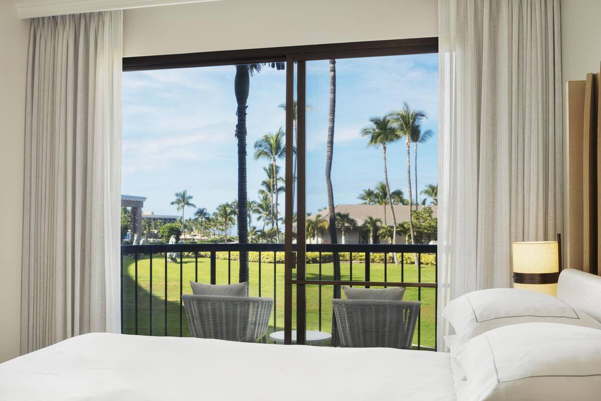 Une chambre d’hôtel avec un balcon, un lit, deux chaises et une lampe.