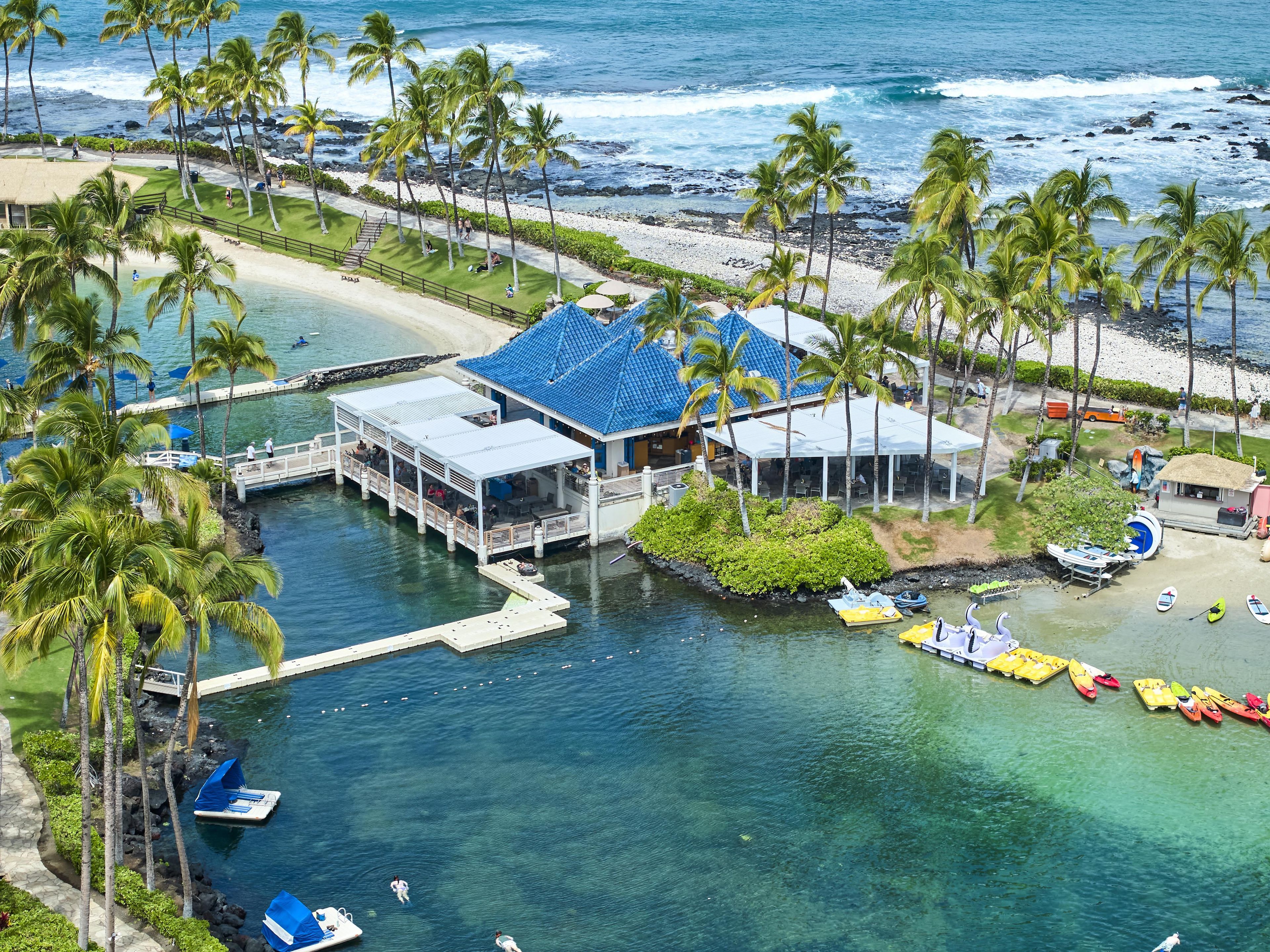 A coastal resort with a dock, water activities, and a building with a blue roof.
