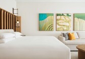 A hotel room with a bed, a sofa, and two paintings on the wall.