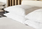 A neatly made bed with white linens and a modern headboard with vertical wooden slats.