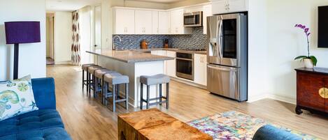 A modern kitchen with stainless steel appliances, a bar area, and a seating space with a blue sofa and wooden coffee table.